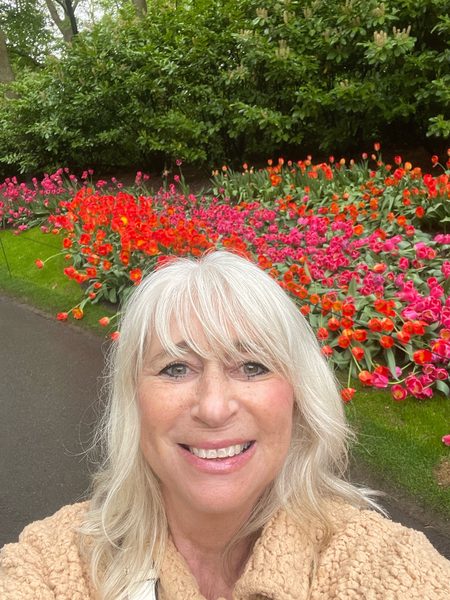 Karen smiling in a selfie in front of beds of red and pink tulips at Keukenhof