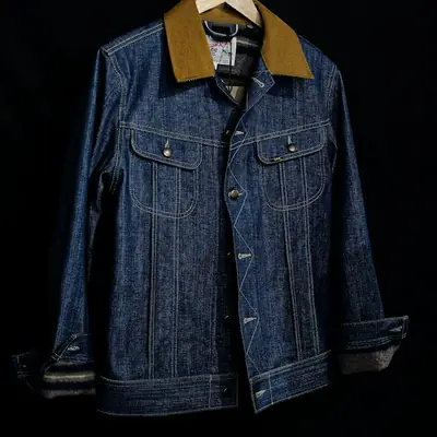 A dark denim jacket with a cord collar on a hanger
