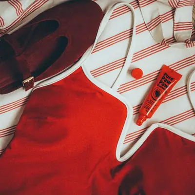 A red swimsuit and sun cream on a striped beach towel